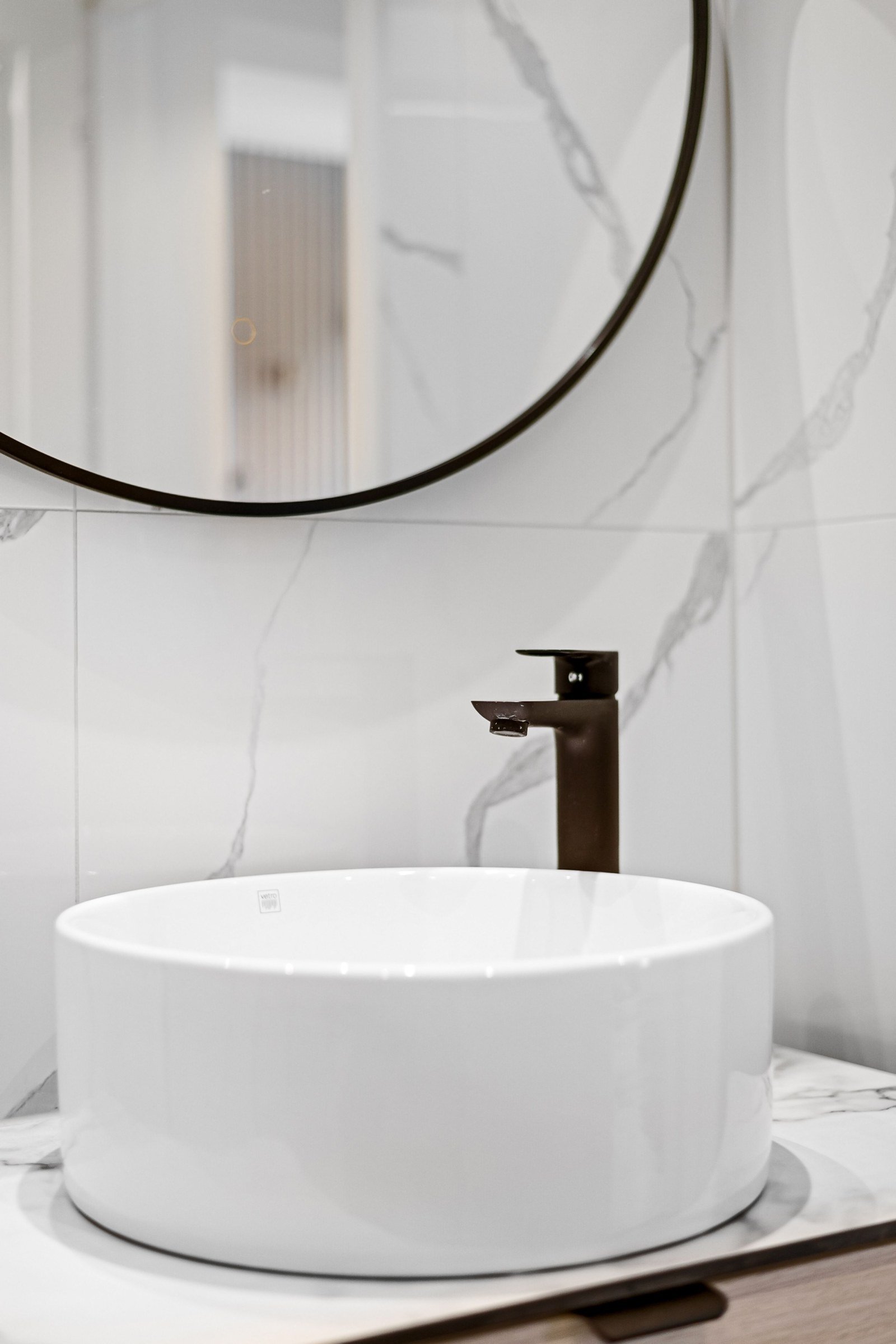 Round white vessel basin and dark faucet below a circular mirror