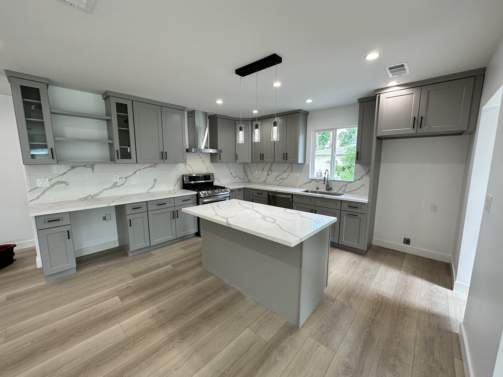 Gray kitchen cabinets and island with light counters, pendant lights and unfilled appliance spaces