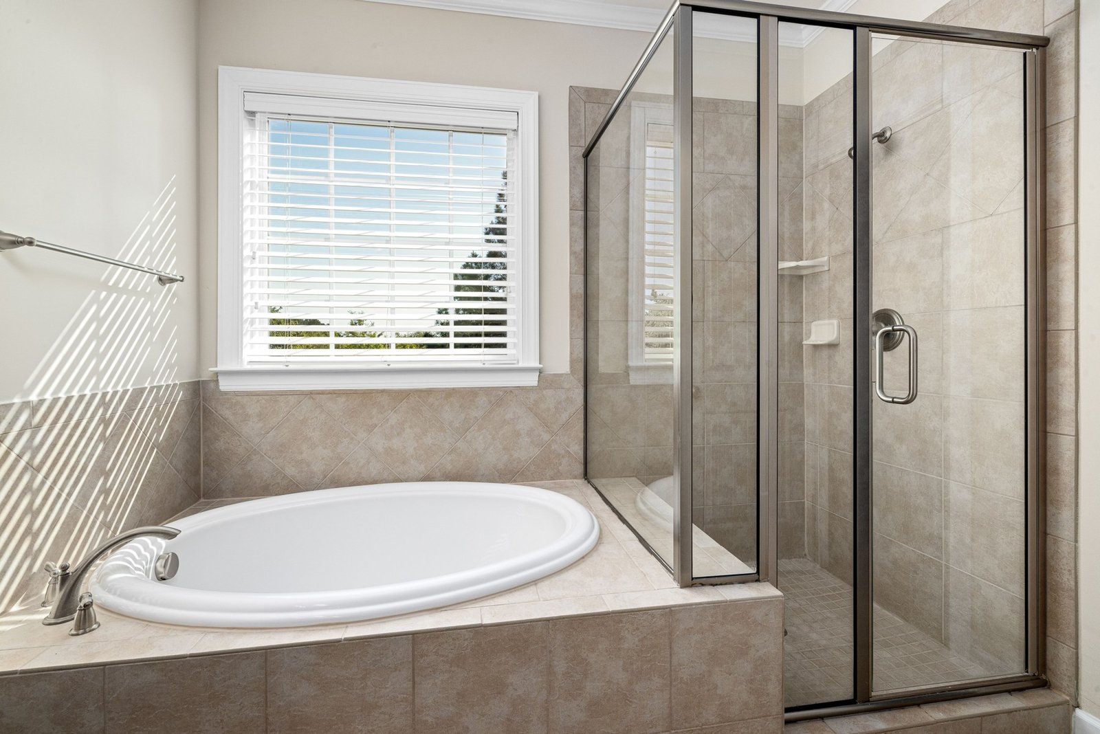 Tiled bathtub beside a glazed shower enclosure and window with blinds