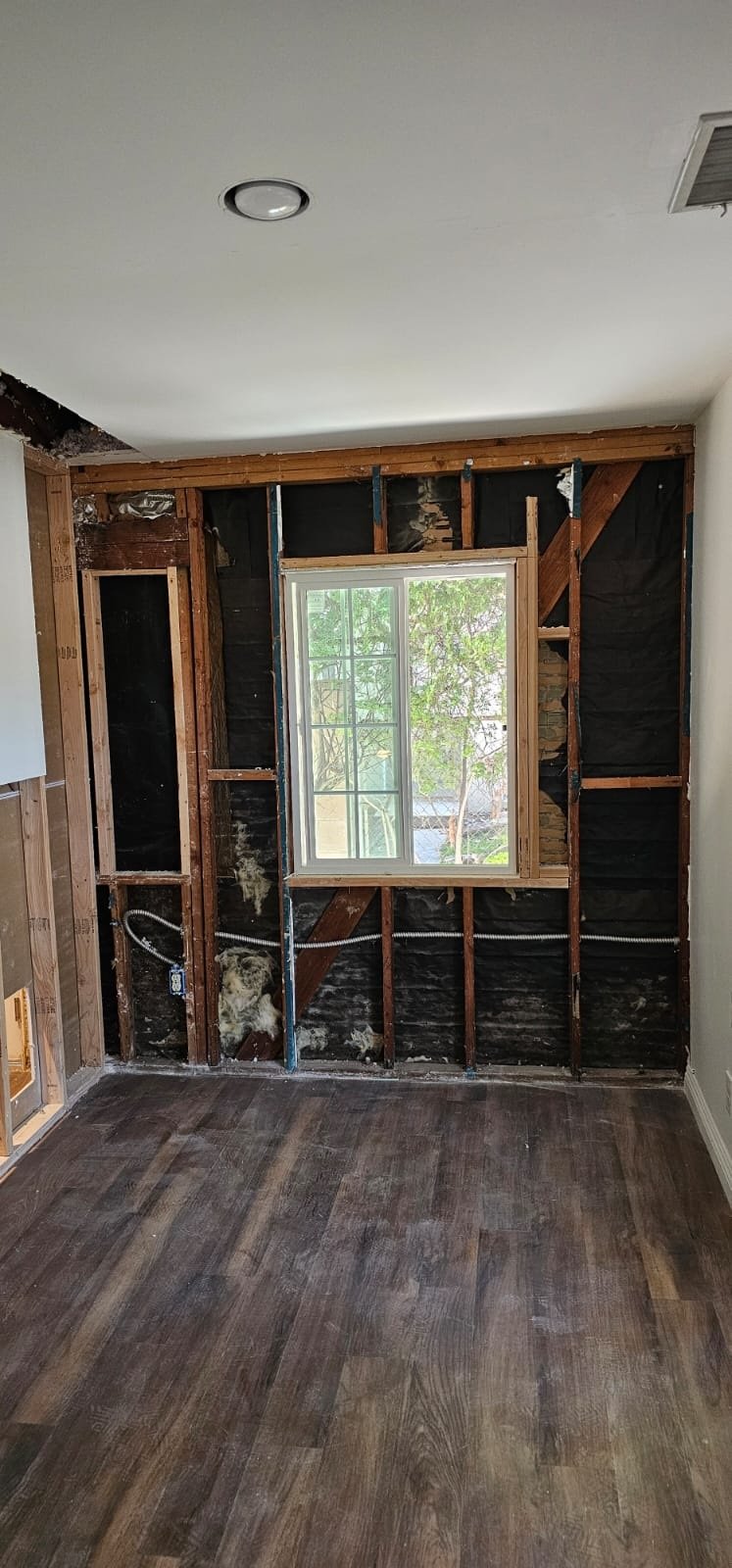 Existing window surrounded by exposed wood studs, diagonal wood bracing and visible wall-cavity material