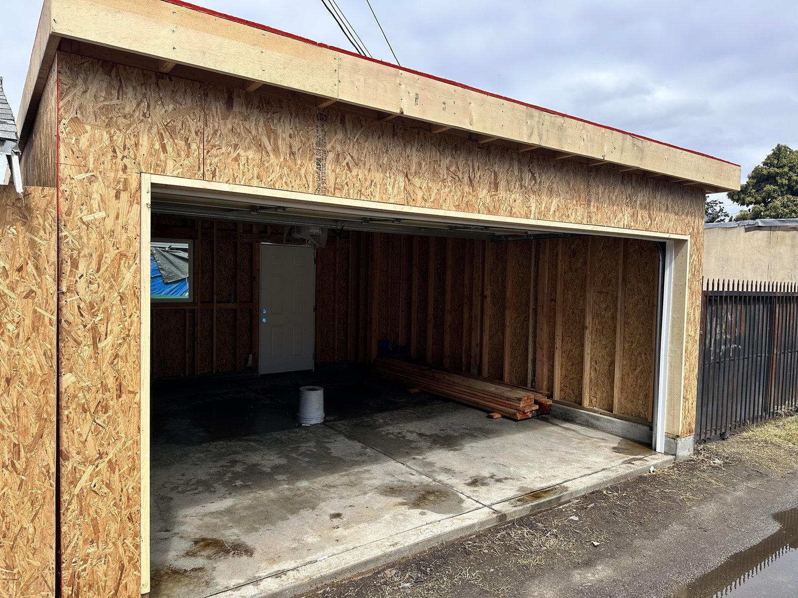 Open garage bay with exposed wood sheathing, wood studs, concrete floor and stored lumber
