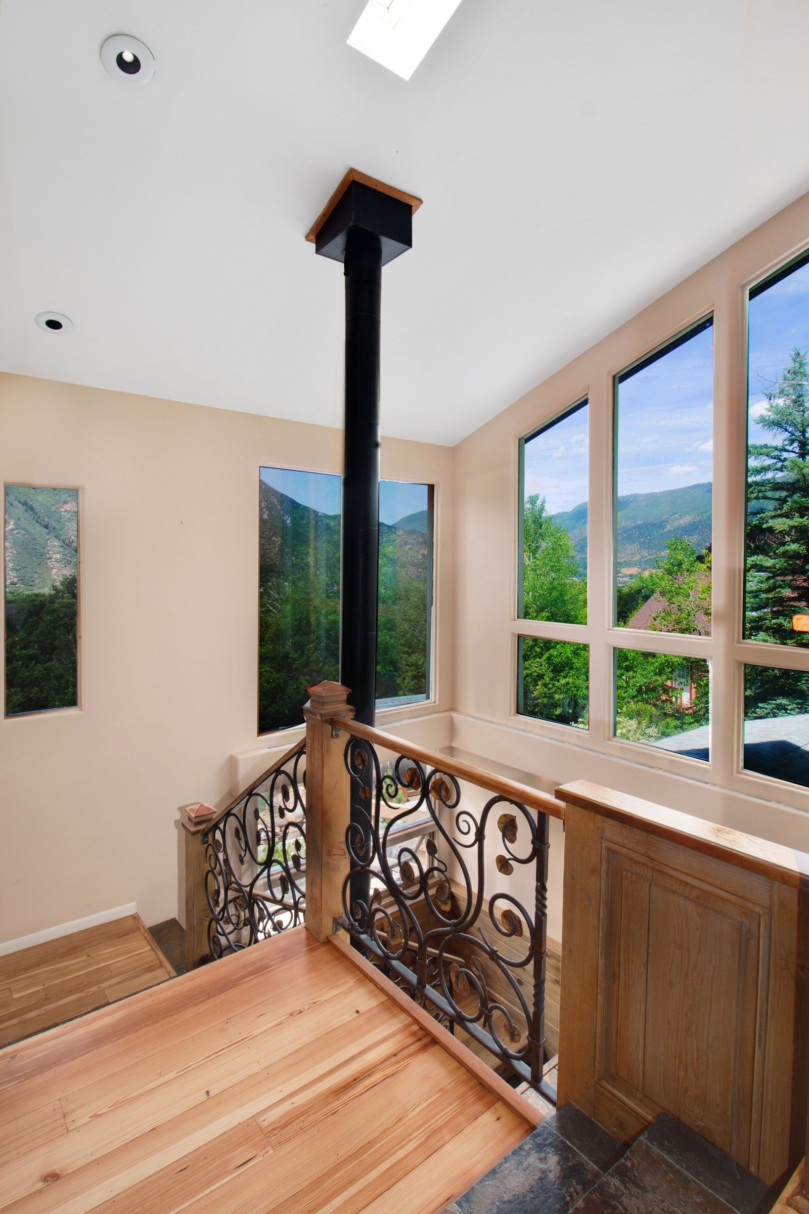 Wooden stair landing with decorative railing beside large windows and a black flue