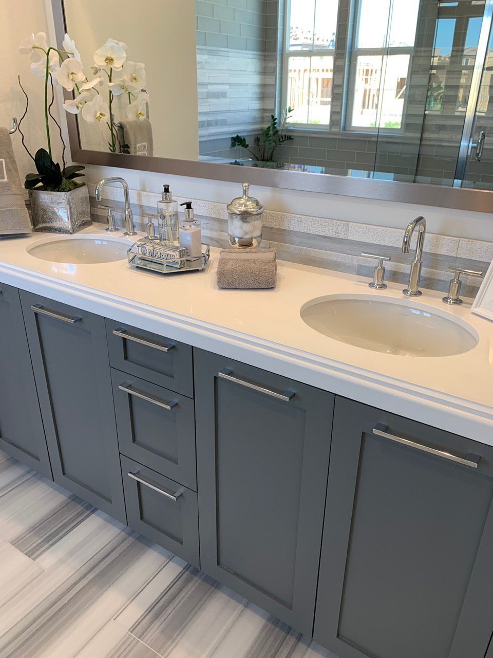 Double vanity with two basins, blue-gray cabinet doors and a large mirror reflecting a shower and window