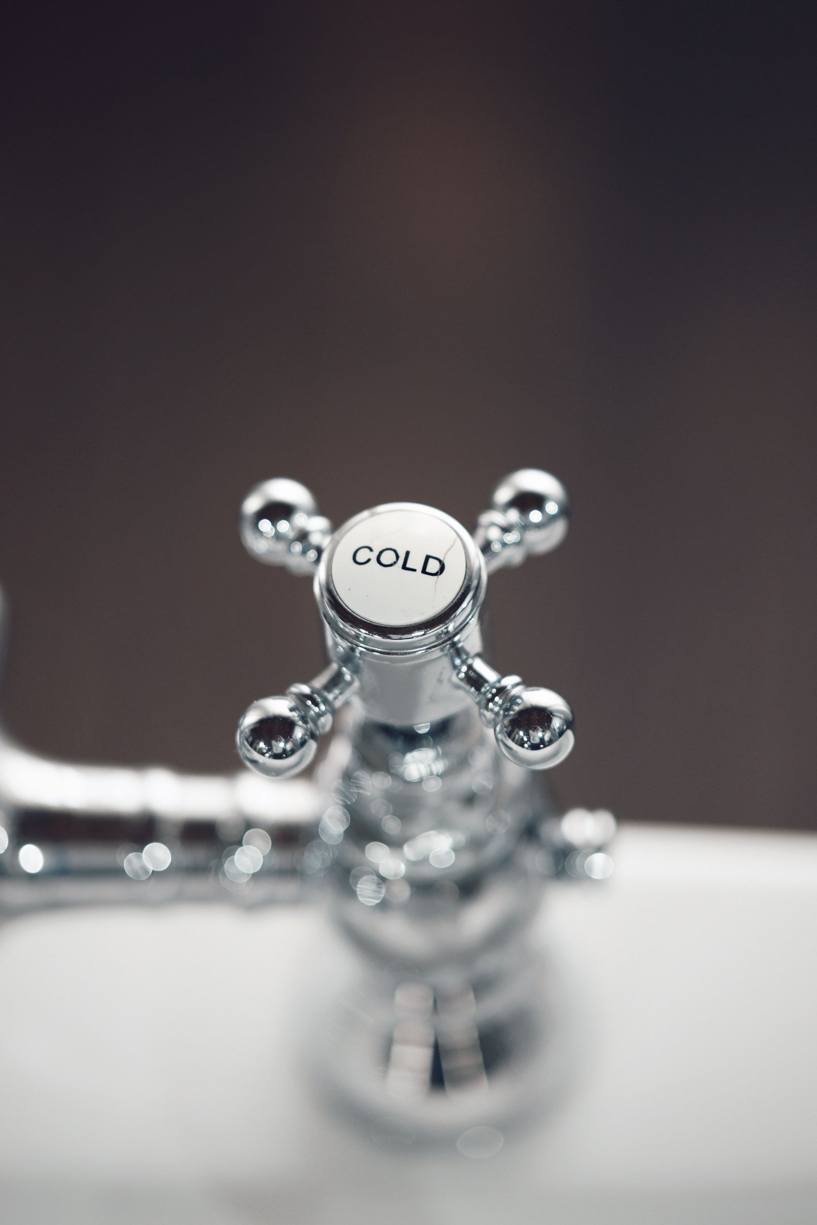 Close-up of a chrome cross-shaped faucet handle marked Cold