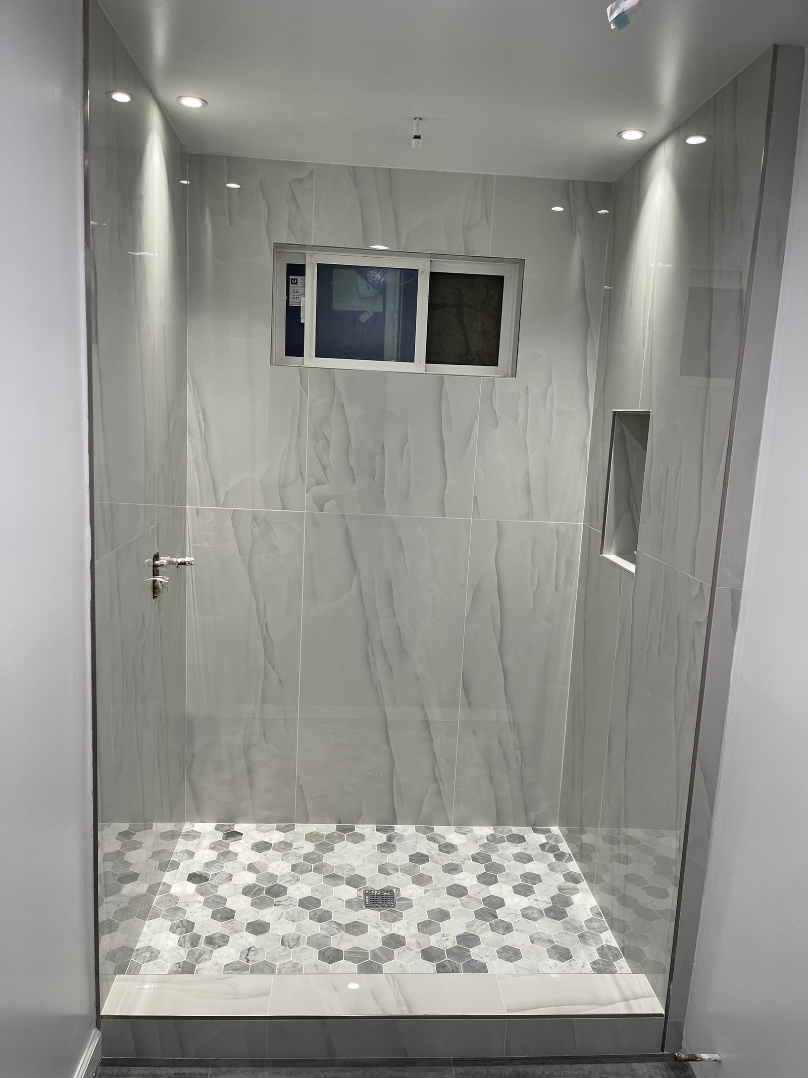 Large gray-veined shower wall tiles beside a recessed niche and hexagonal floor mosaic