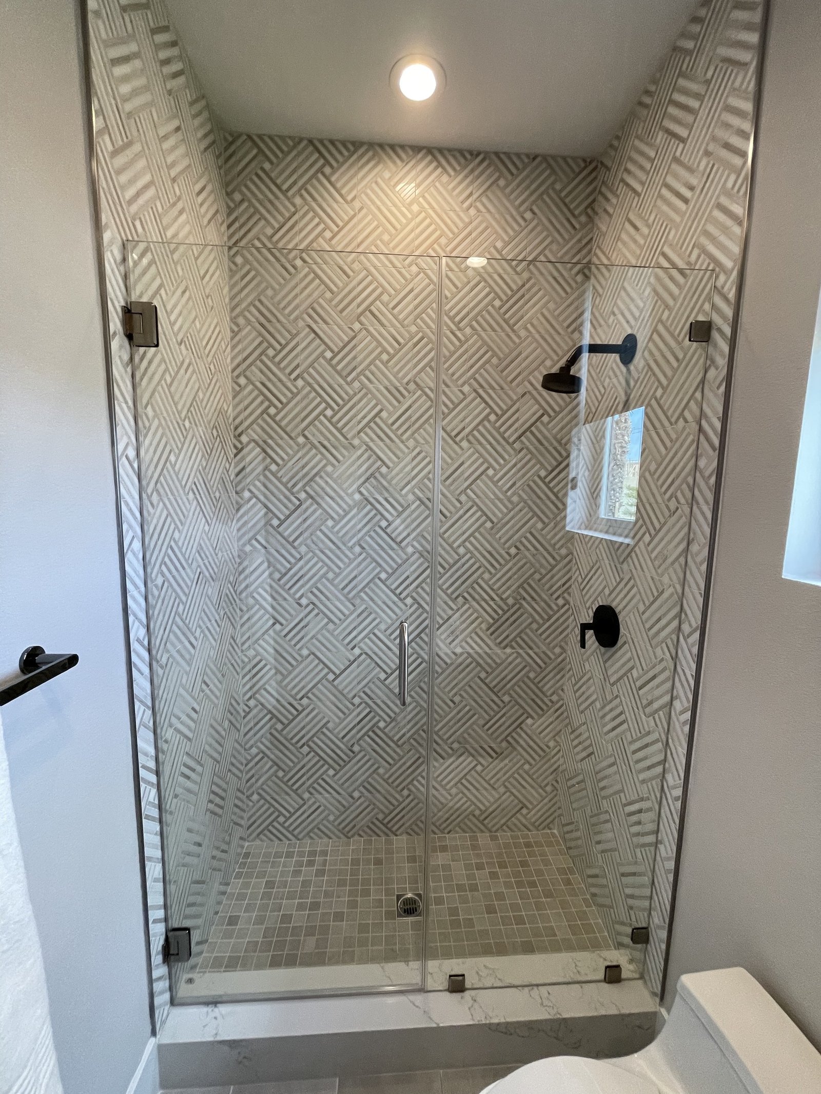 Glass-enclosed shower with patterned wall tiles, small square floor tiles and dark fixtures