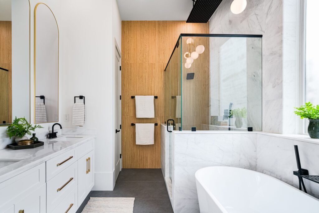 Bright bathroom with a glass shower enclosure, pale wall surfaces, dark floor tile and a freestanding tub