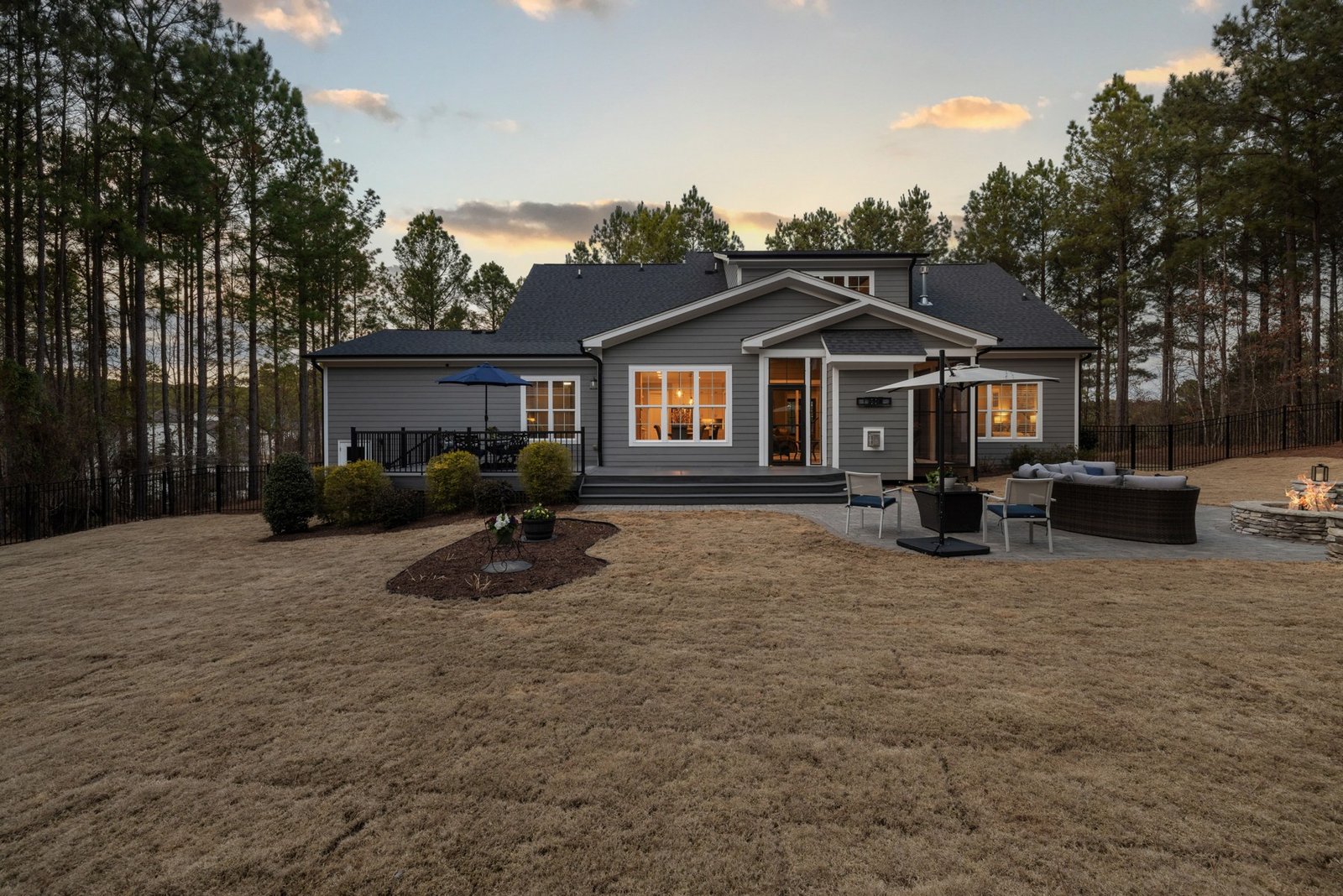 Rear of a sided house with illuminated windows, a deck, patio seating and lawn