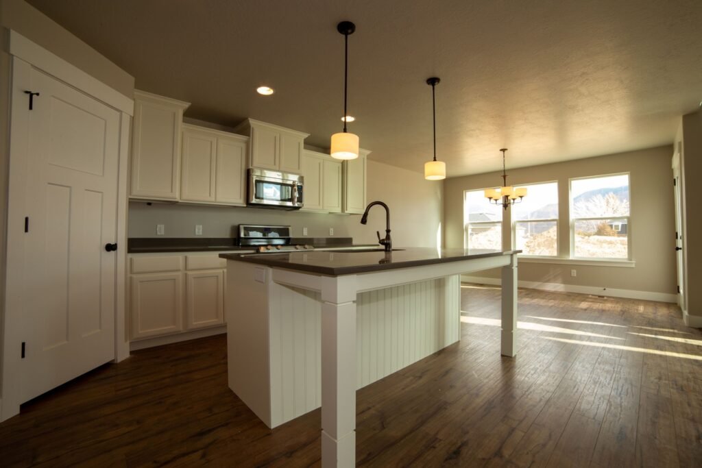 Empty kitchen with a white island, surrounding cabinets and a window-lit dining area