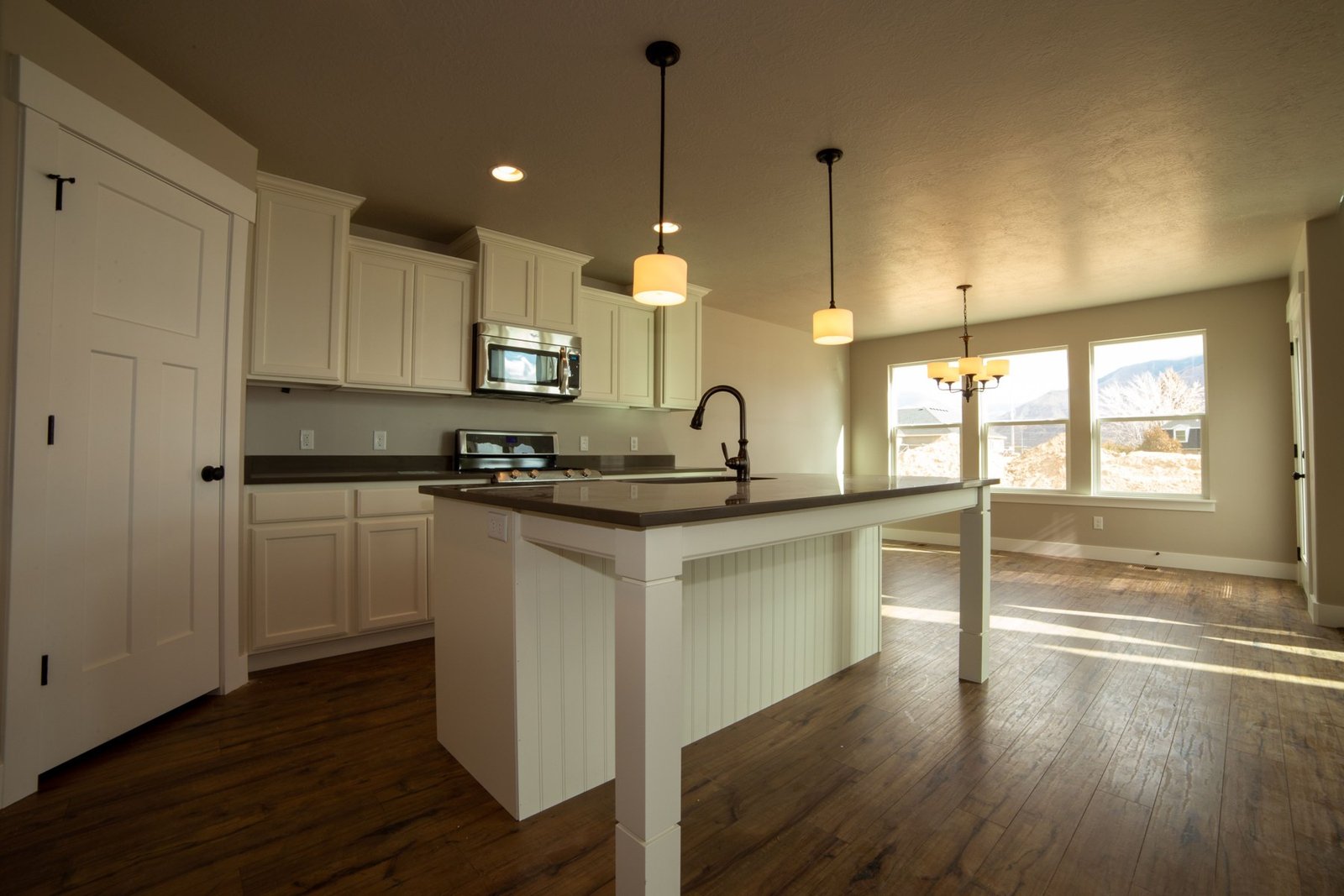 Empty kitchen with a white island, surrounding cabinets and a window-lit dining area