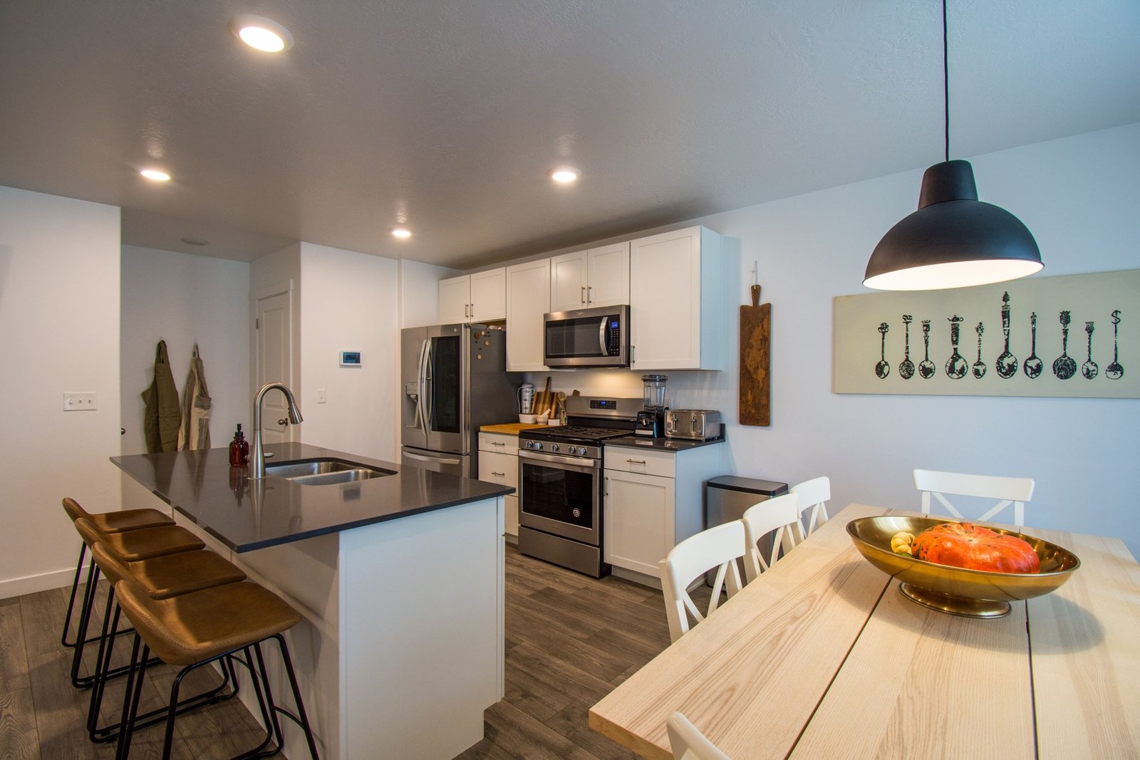 White kitchen island with stools beside a wooden dining table and stainless appliances
