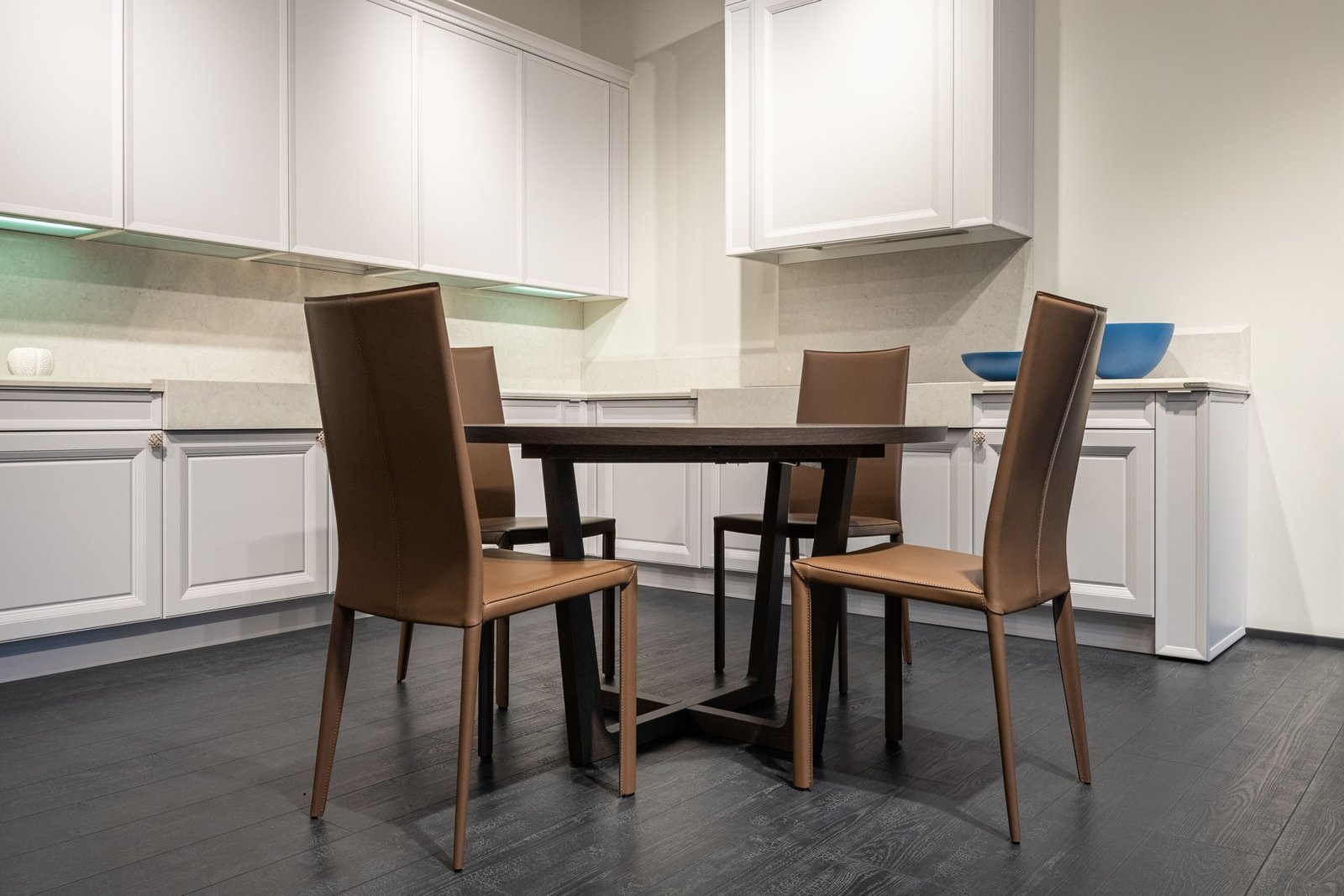 Dark dining table and four brown chairs surrounded by white kitchen cabinets