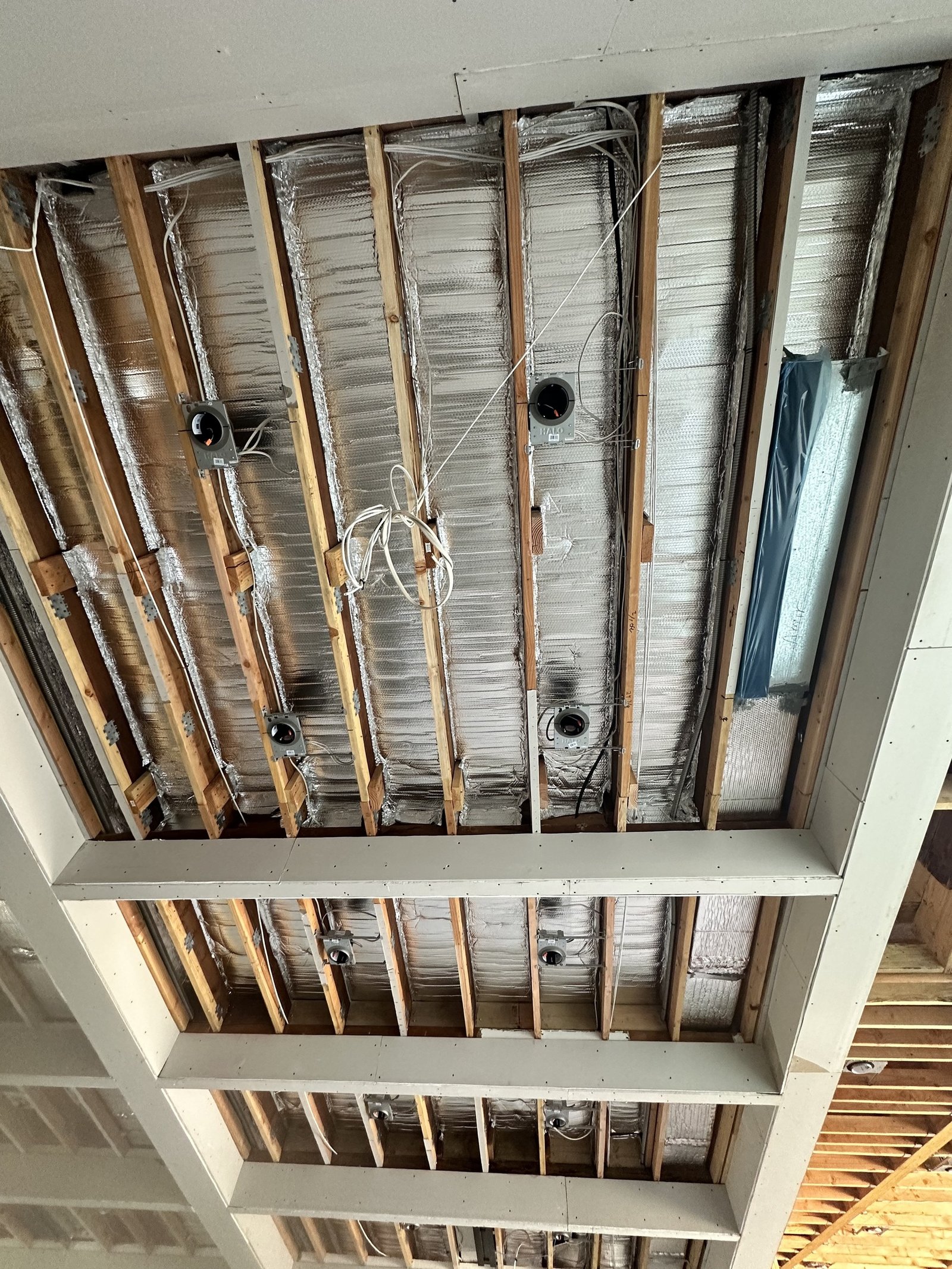 Open wood ceiling framing with recessed-light housings, wiring and foil-faced material