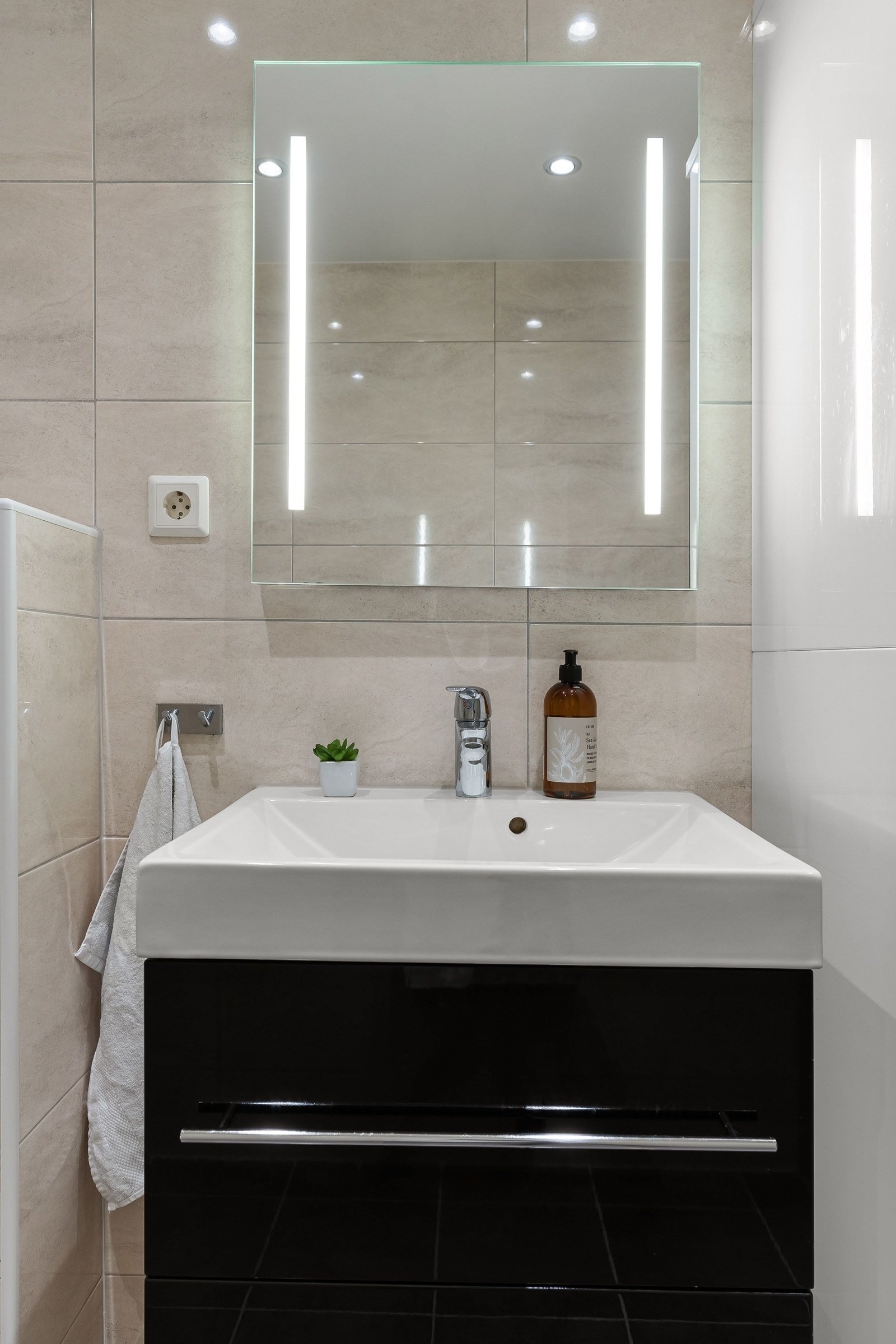 Rectangular bathroom mirror with two illuminated vertical strips above a white basin