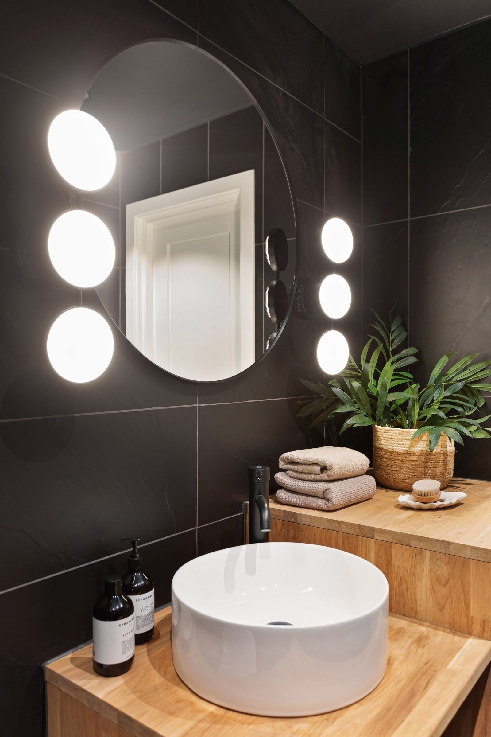 Round bathroom mirror flanked by vertical rows of illuminated globe lights above a basin
