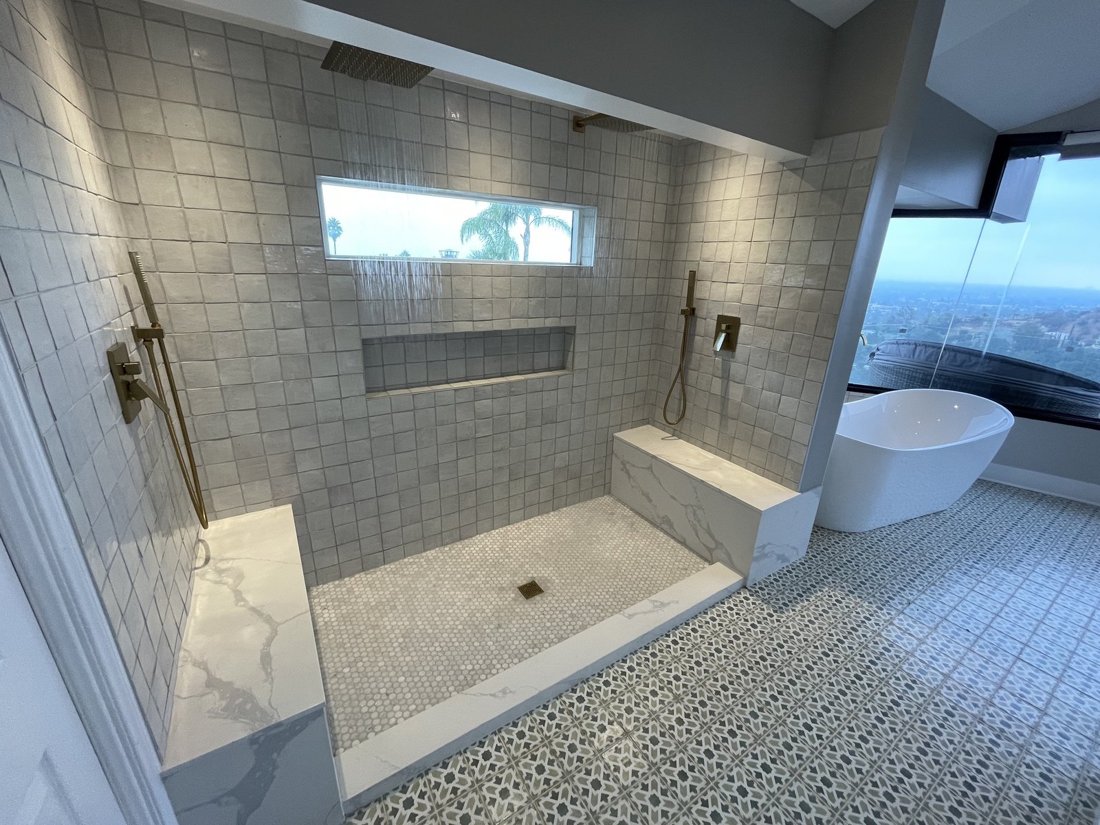 Wide tiled shower with two benches and a freestanding tub beside a large window
