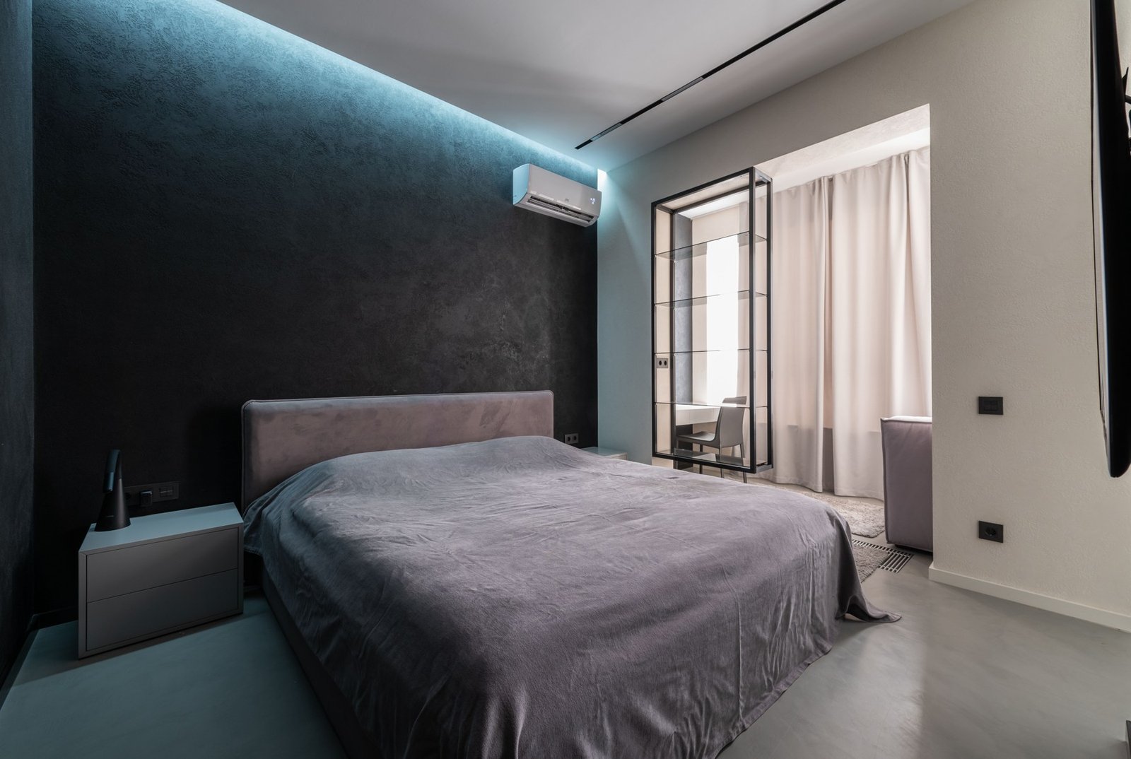 Bedroom with a wall-mounted air-conditioning unit and an open glazed partition beside the bed