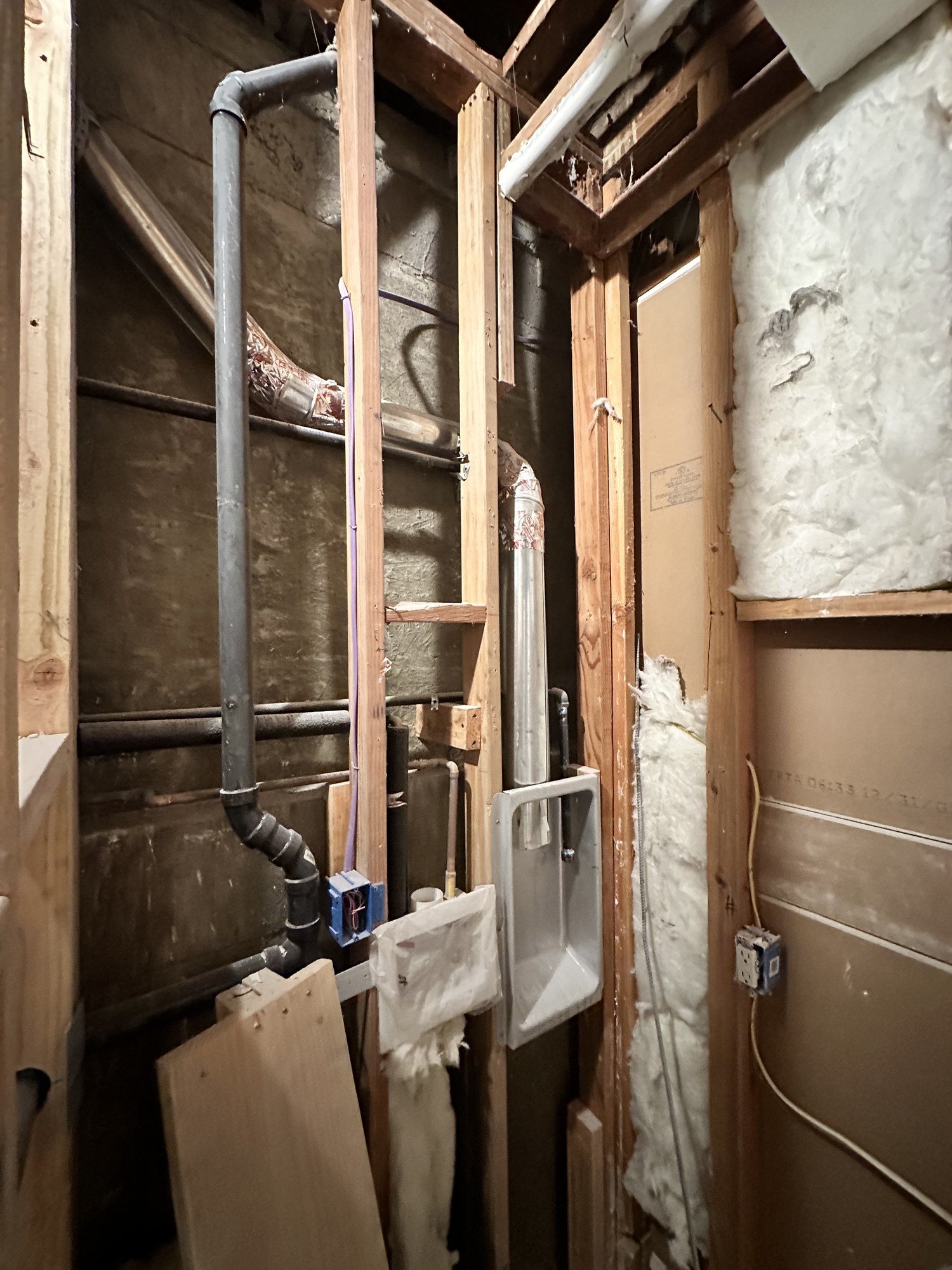 Exposed wood studs with visible piping and service lines in an unfinished wall