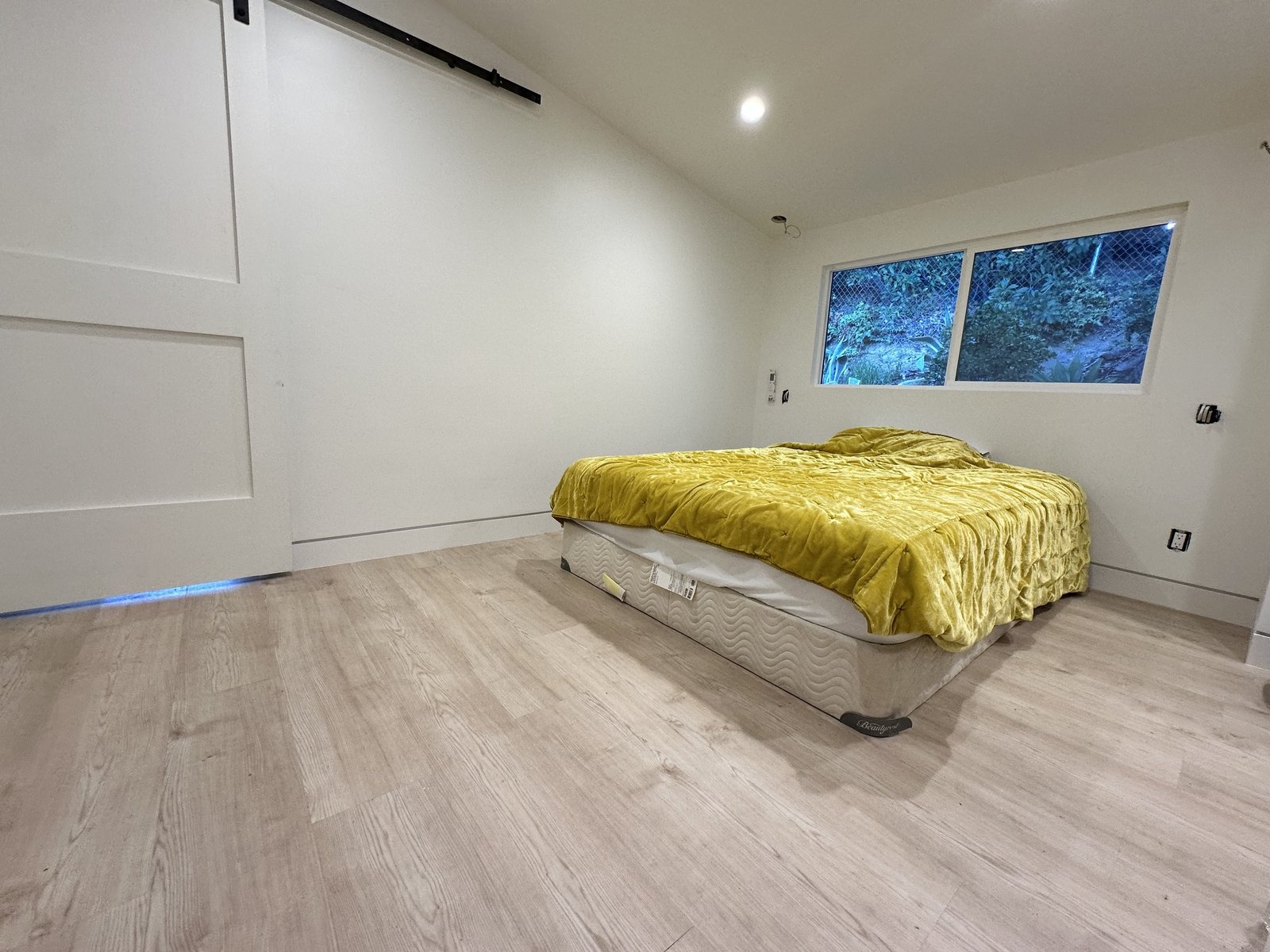 Bedroom during finishing with a bed, broad window, light flooring and a white sliding door
