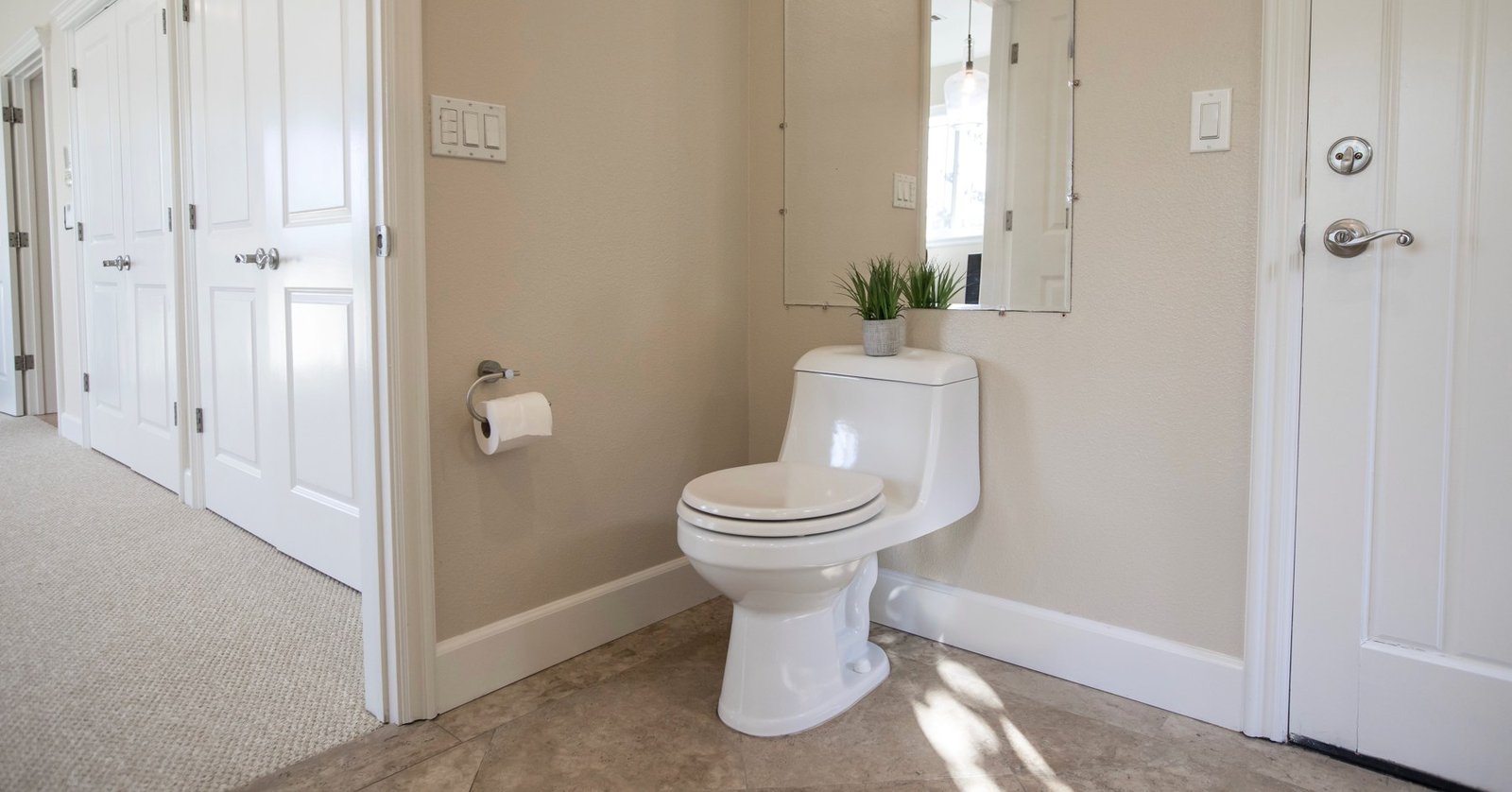 Toilet area with an open doorway to a carpeted hall and a closed door beside the toilet