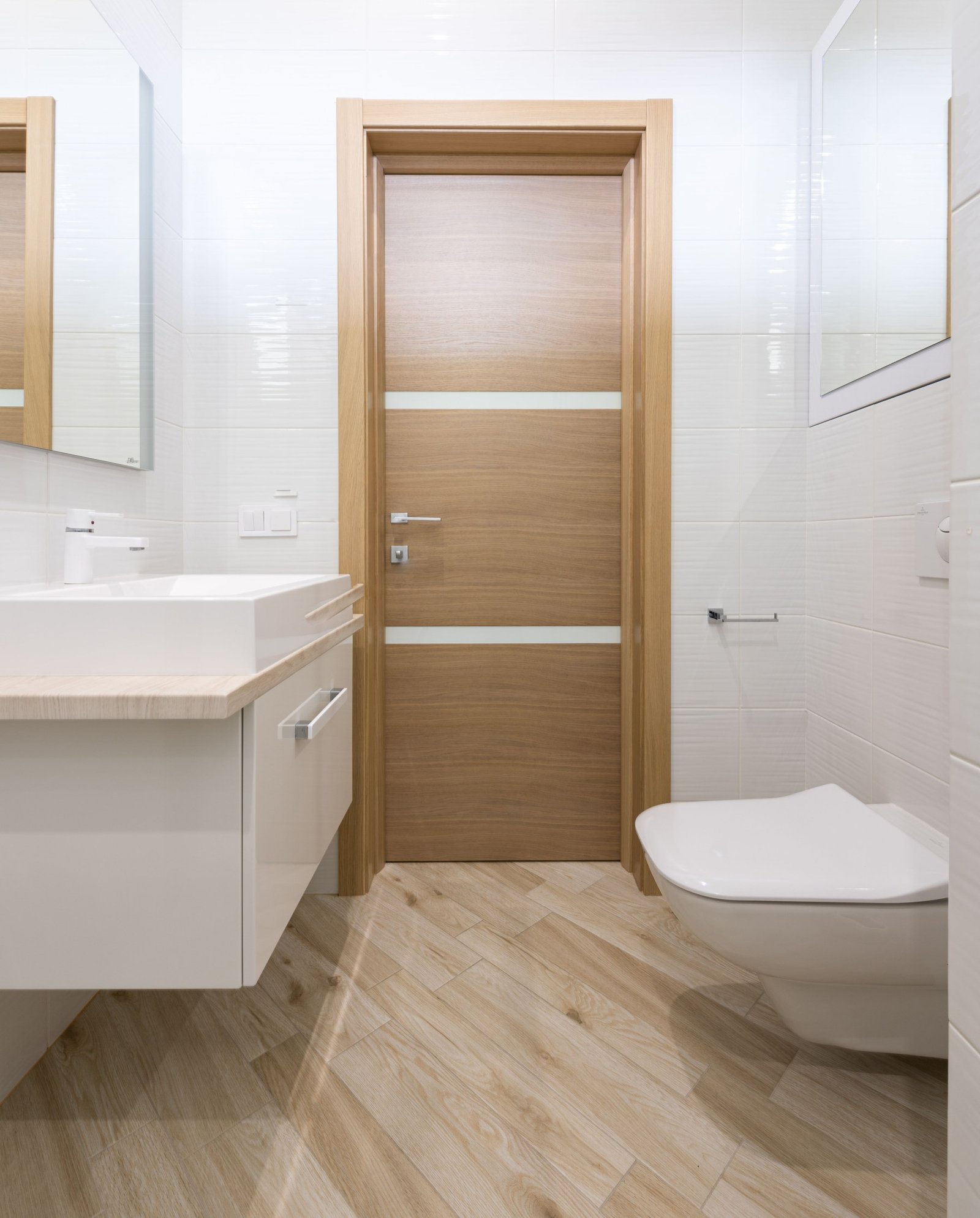 White bathroom with a wood-finish door, wall-mounted basin cabinet and toilet