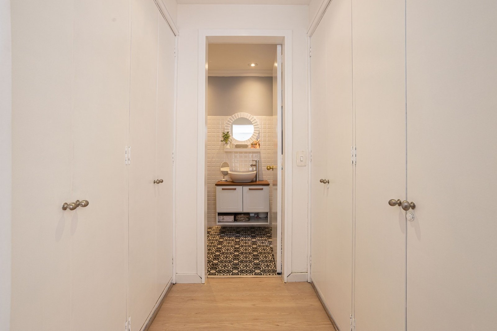 Narrow passage lined with white closet doors leading to an open bathroom doorway