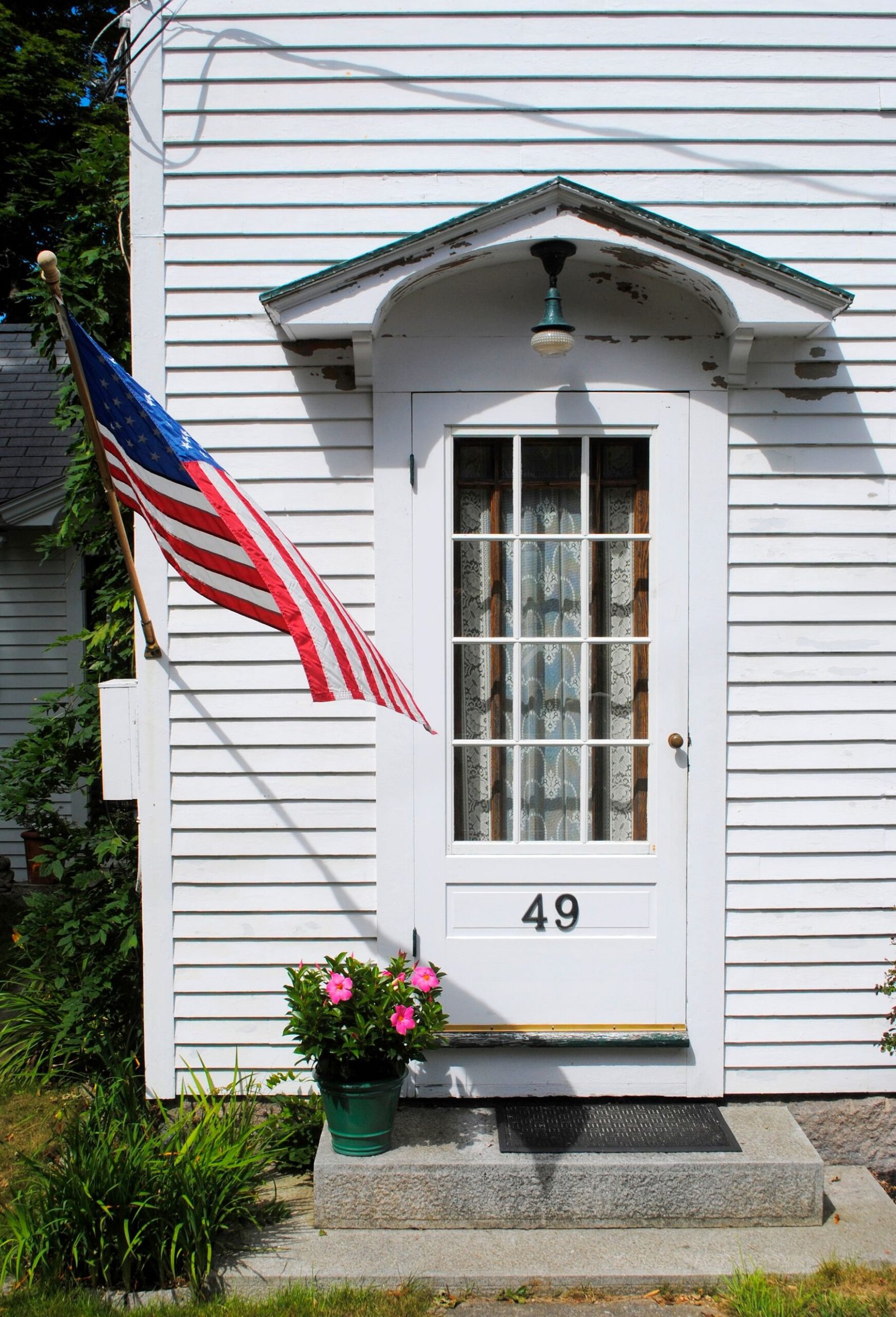 White-sided home entrance with glazed door, small canopy and potted flowers