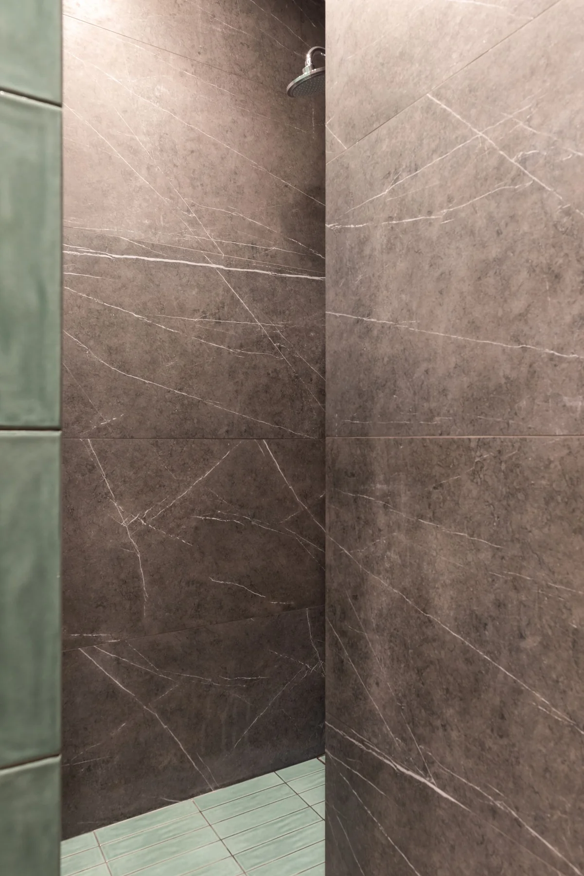 Close view of a finished tiled shower with stone-pattern walls, a showerhead and green floor tiles.