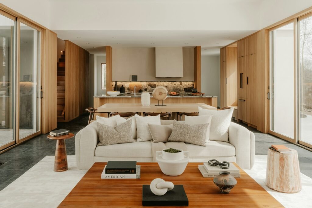 Connected living, dining and kitchen areas with a cream sofa, wood cabinetry and large windows.