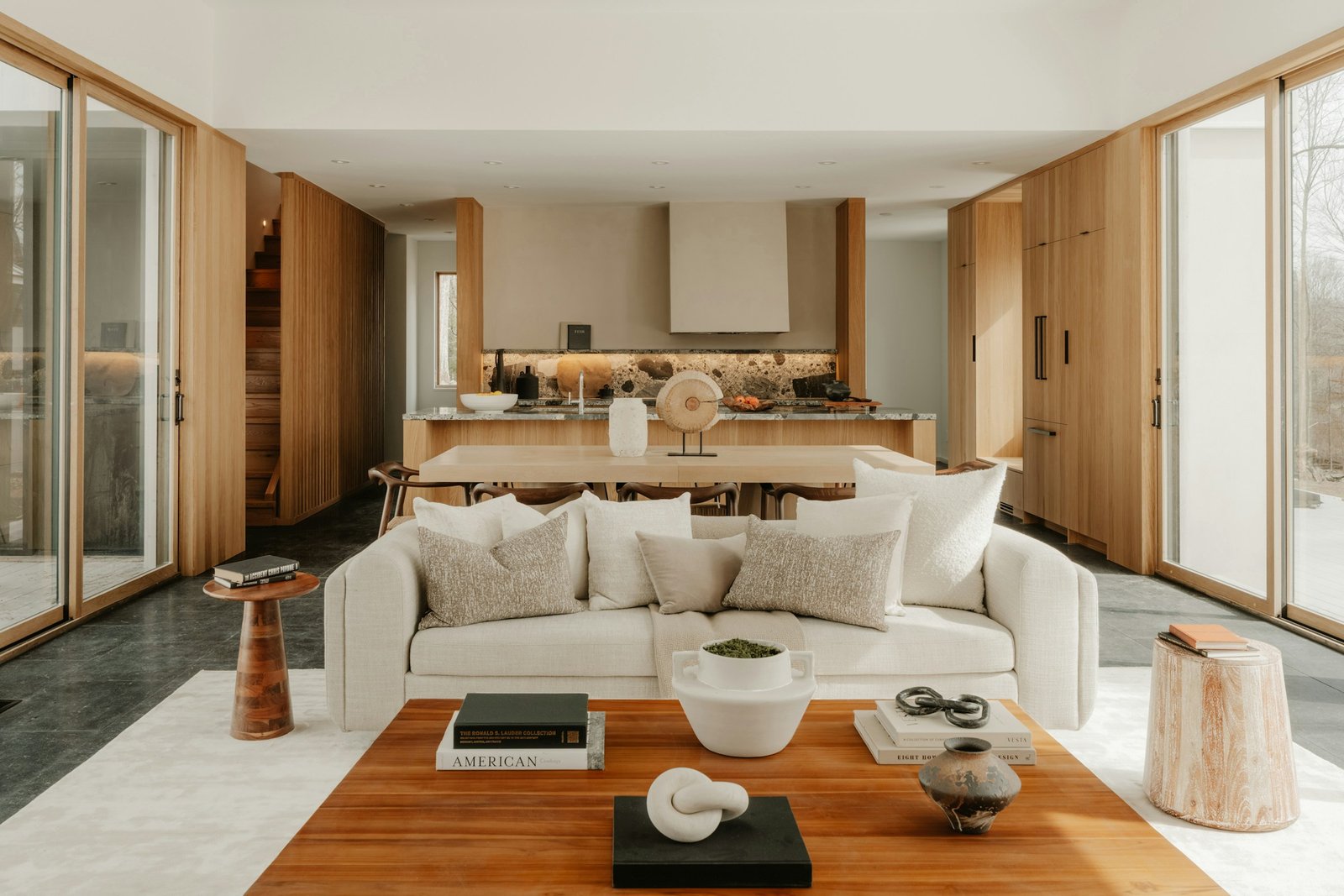 Connected living, dining and kitchen areas with a cream sofa, wood cabinetry and large windows.